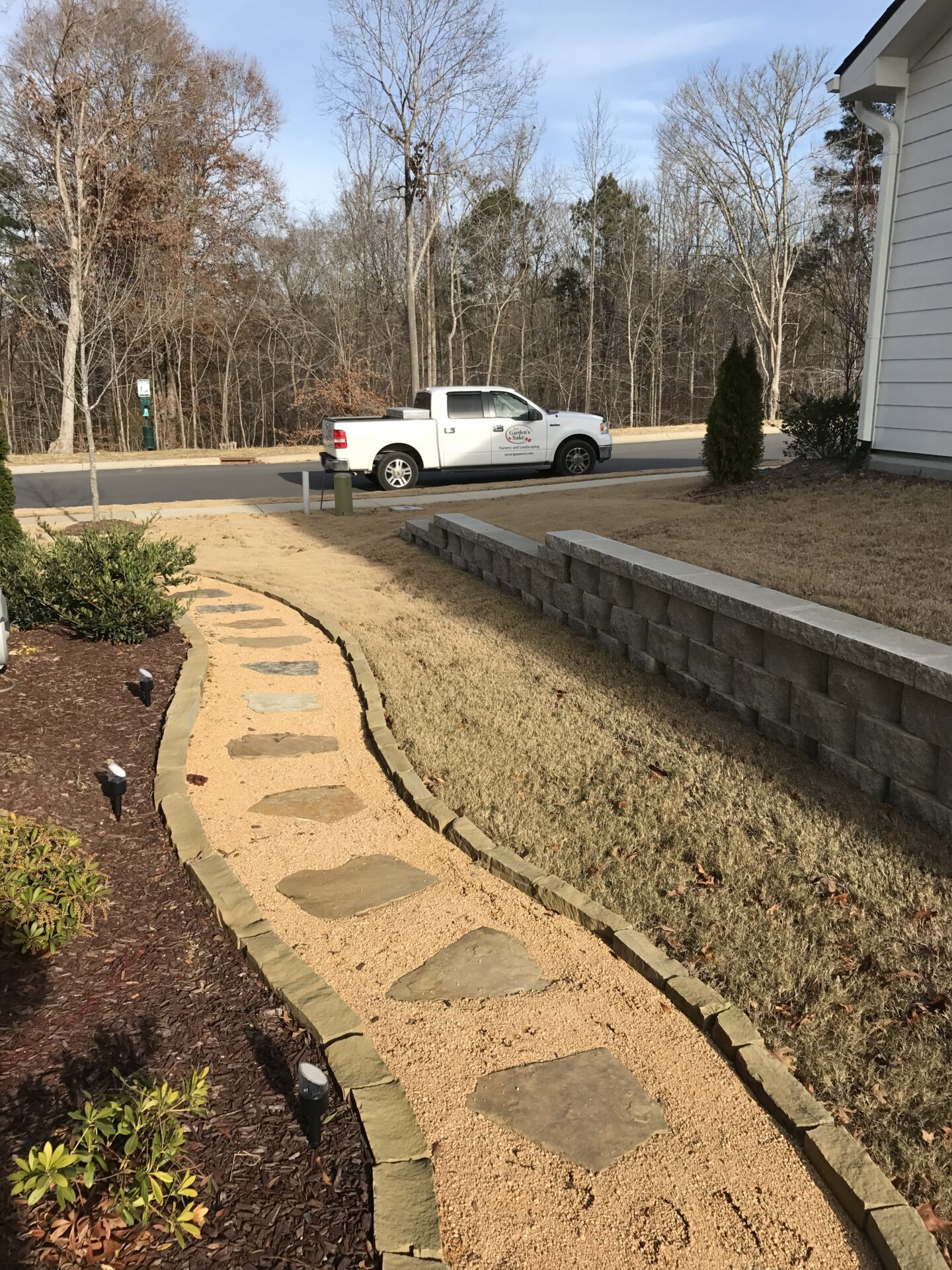 A winding stone path leads to a parked truck near a house. Trees line the background, and there are no recognizable landmarks.