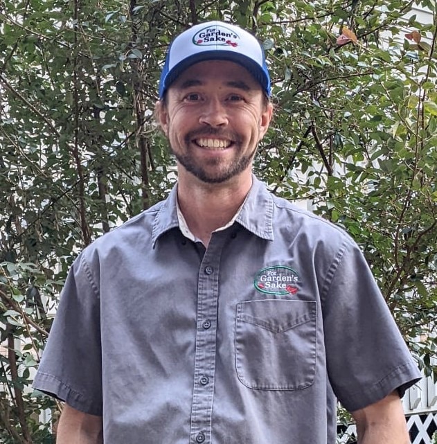 A person wearing a "Garden's Sake" cap and shirt stands outdoors. Green foliage is visible in the background.