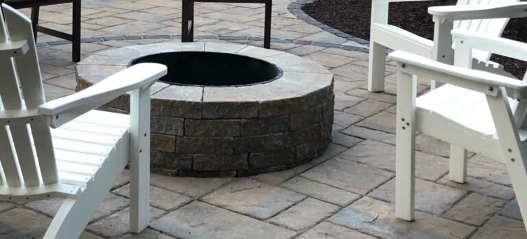 Four white chairs surround a circular stone fire pit on a tiled patio. The area appears serene and ready for social gatherings.