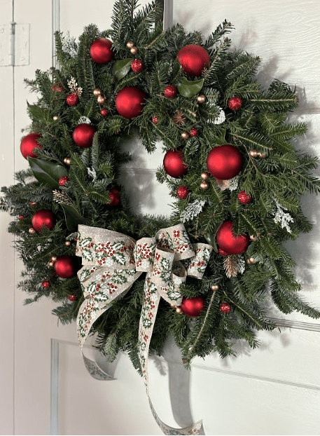 Festive Christmas wreath adorned with red ornaments, pine cones, and a decorative bow, hanging on a light-colored door.