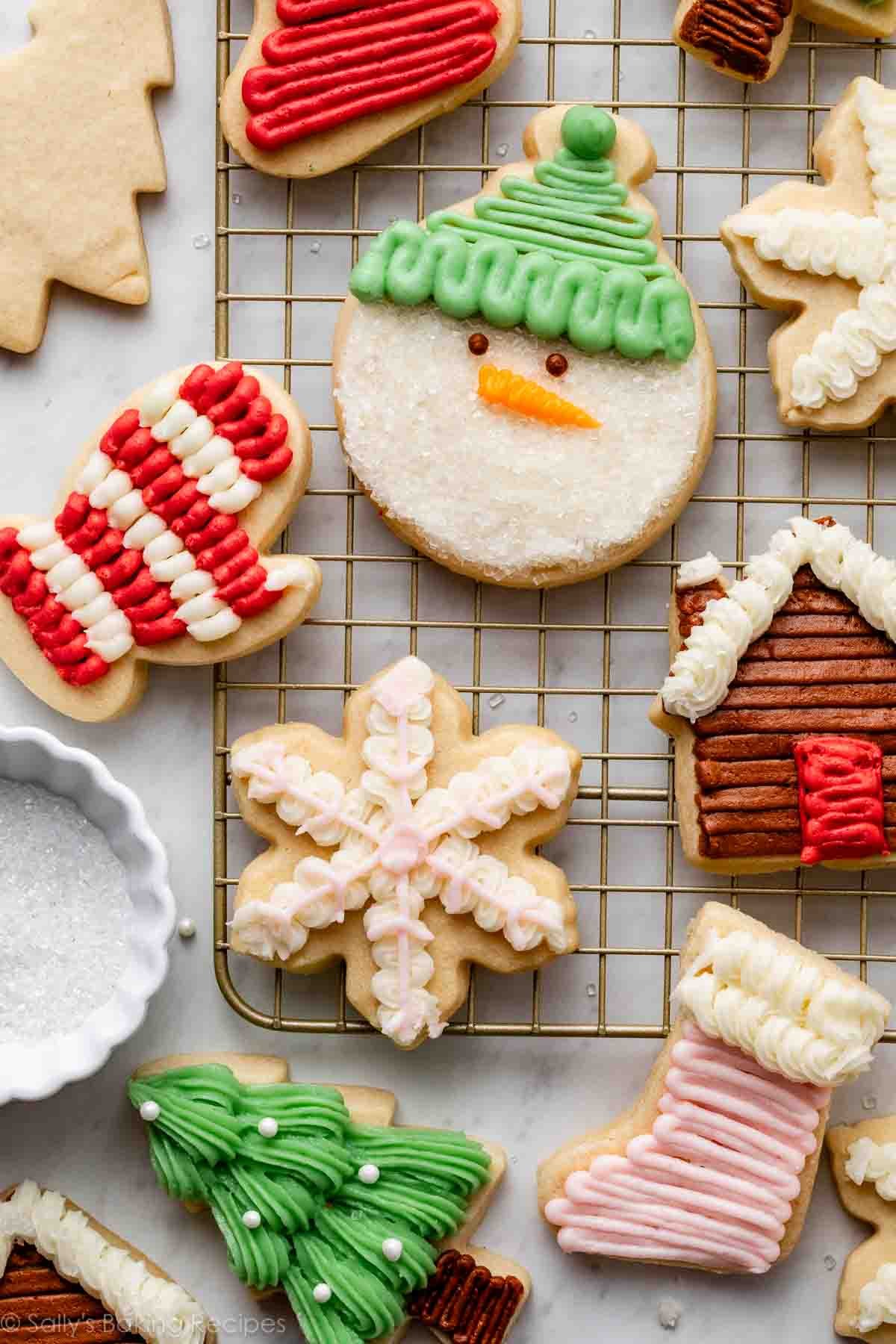 Festive cookies shaped like snowmen, mittens, snowflakes, and trees, decorated with colorful icing on a cooling rack. Festive holiday baking ambiance.