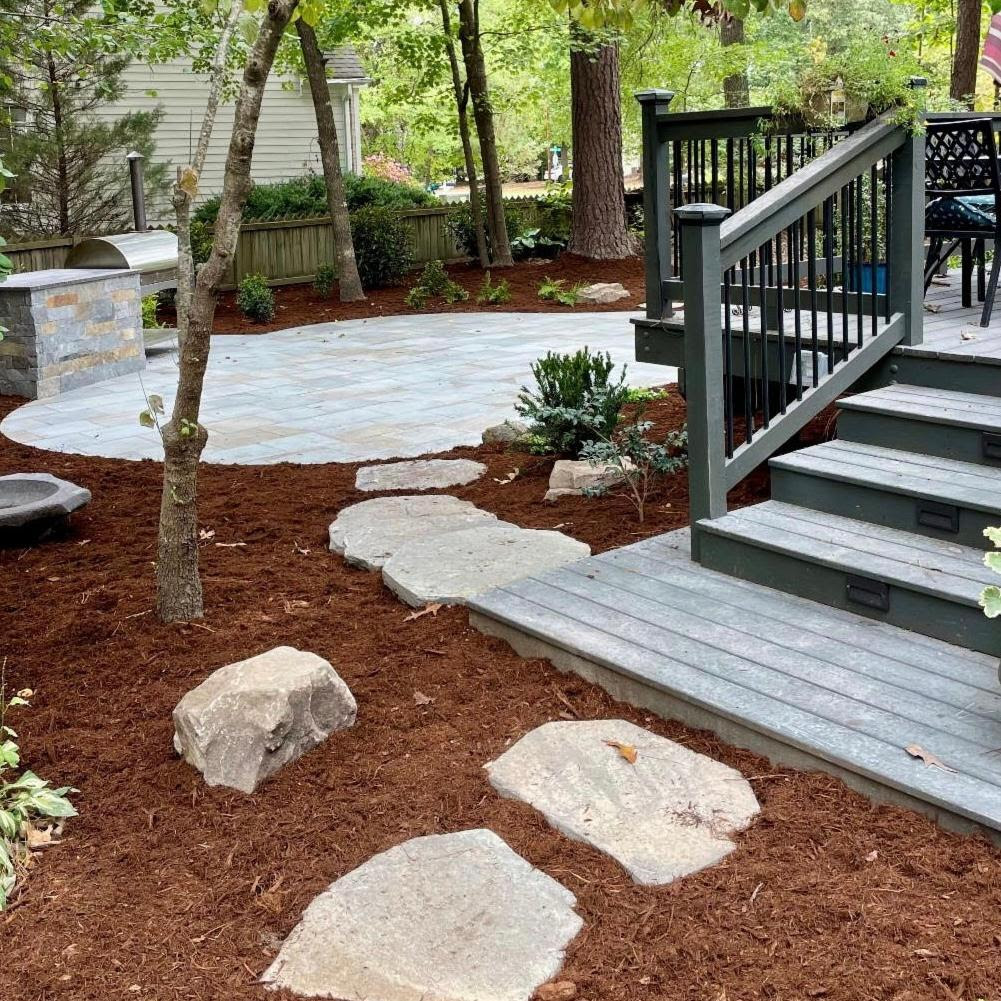 A serene backyard patio features stone steps, wooden decking, and surrounding trees, creating a peaceful, natural outdoor space with a cozy, landscaped atmosphere.